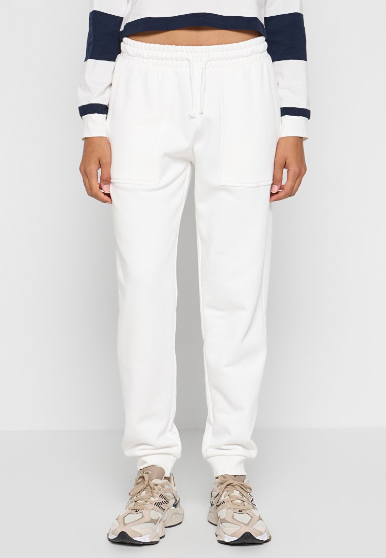 Weiße Baumwoll-Sweatpants mit elastischem Bund, zwei Seitentaschen und zulaufenden Beinen. Kombiniert mit beigen Sneakers mit schwarzen Akzenten.
