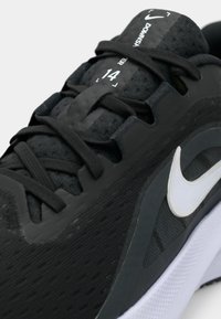 Μαύρο αθλητικό παπούτσι με επάνω μέρος από διχτυωτό υλικό, λάστιχα από καουτσούκ και άσπρο λογότυπο. Διαθέτει μαλακή σόλα και έντονο σύστημα κορδονιών. Το μέγεθος είναι σημειωμένο ως 14.