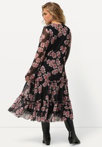 Vestido negro de flores con mangas largas transparentes, falda de volantes en capas y patrones florales en rosa; combinado con botas negras hasta la rodilla.