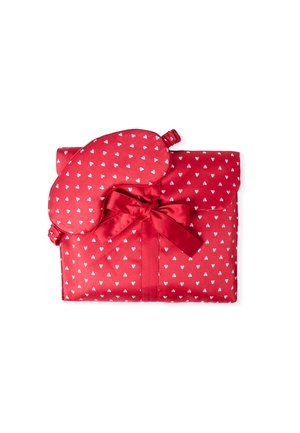 Conjunto de dormir de tela roja que incluye una máscara para dormir y una bolsa. Los materiales son satén suave con pequeños patrones de corazones blancos. Atado con un lazo a juego.