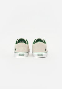 Beige suede sneakers with green accents, white rubber soles, and a logo on the heel. Low-top design, rounded toe, and padded collar.