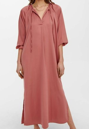 Mujer con un vestido largo suelto de color rosa polvoriento, con mangas tres cuartos, aberturas laterales, escote en V y lazos decorativos en el cuello.