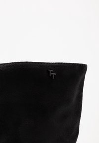 Svart konstläder stövlar med en mjuk textur, med en rundad topp och en liten svart logotypdetalj på sidan.