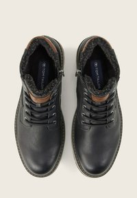 Botas de cuero negras con forro de felpa gris, acentos de cuero marrón y ojales de metal. Cierre de cremallera en el lateral para una fácil puesta.