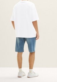 Camiseta blanca de gran tamaño con mangas cortas, combinada con pantalones cortos de mezclilla azul. Modelo con zapatillas blancas y calcetas de longitud media.