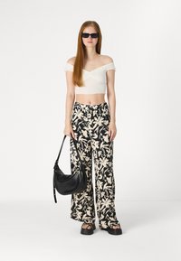 White off-shoulder cropped top with textured fabric, paired with black and cream floral patterned wide-leg pants. Model holds a black bag.