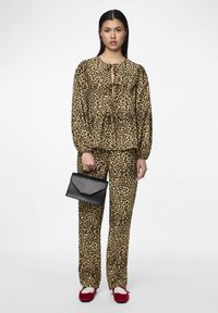 Πυτζάμες με λεοπάρ σχέδιο σε καφέ και μαύρο, με άνετη γραμμή και ελαστική μέση, συνδυασμένες με μία μαύρη τσάντα φάκελο και κόκκινα παπούτσια.