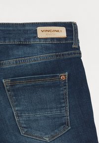 Jeans z denimu w ciemnym niebieskim kolorze z skórzaną metką z napisem "VINGINO". Posiadają tylnią kieszeń z mosiężnymi nitami i kontrastowym szwem.