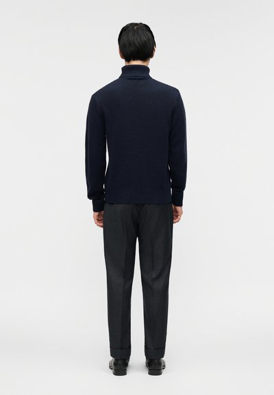 Σκούρο μπλε πλεκτό πουλόβερ με ψηλό γιακά, συνδυασμένο με γκρι ριγέ παντελόνια και μαύρα παπούτσια, θέα από πίσω. Λείο υλικό.