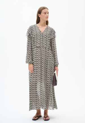Maxikleid aus schwarz-weißem gemustertem Stoff, mit V-Ausschnitt, langen Ärmeln und Rüschendetails; kombiniert mit einer Clutch und Sandalen.