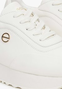 Białe sneakersy wykonane z gładkiej skóry, z okrągłymi sznurówkami, zaokrąglonym noskiem i złotym logo na boku. Płaska, teksturowana podszewka.