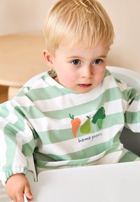 Grön och vit randig vattentät haklapp med tecknade grönsaker (morot, päron, broccoli) och texten "hemodlad", mjuk textur.
