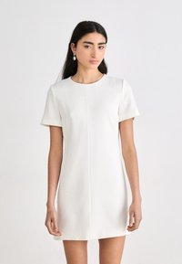 Bílé šaty s krátkým rukávem, kulatým výstřihem, přiléhavým střihem a čistými švy. Hladká látka s minimalistickým designem a bez viditelných vzorů.
