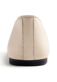 Zapato de cuero beige con punta redonda y suela baja negra. Presenta costuras visibles en la parte trasera y una textura suave.