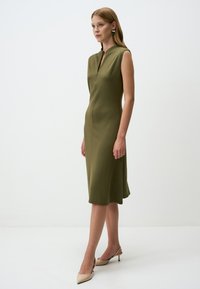 Olivengrünes Kleid in knielanger Länge mit hohem Kragen, ärmellosem Design und dezenter A-Linie, aus glattem, elastischem Stoff gefertigt.