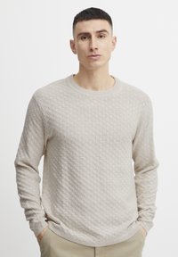 Beige knitted sweater featuring a textured pattern, round neckline, and long sleeves. Soft material with ribbed cuffs and hem.