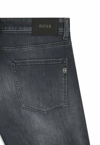 Jeans de mezclilla oscura con un parche de cuero negro texturizado etiquetado "BOSS", con un diseño sencillo del bolsillo trasero y detalles en metal plateado.