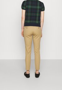 Top azul marino a cuadros con mangas cortas abullonadas, combinado con pantalones ajustados beige y zapatos negros sin cordones, visto desde atrás.