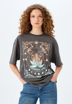 T-shirt gris surdimensionné présentant un design graphique coloré d'une fille et d'éléments célestes, avec un col rond et des manches courtes.