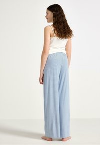 Helle blau gestreifte weite Hose mit elastischem Bund, gefertigt aus einem weichen, leichten Stoff. Das Modell wird von hinten gezeigt, barfuß.