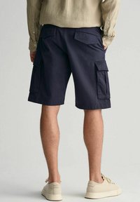 Marinefarbene Cargo-Shorts aus strapazierfähigem Material, mit seitlichen und hinteren Taschen, geradem Schnitt und gesäumten Kanten. Getragen mit beigen Sneakers.