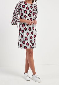 Robe à manches courtes blanche avec des rayures verticales noires et un imprimé animal rose. Présente des manches évasées et est associée à des baskets blanches.