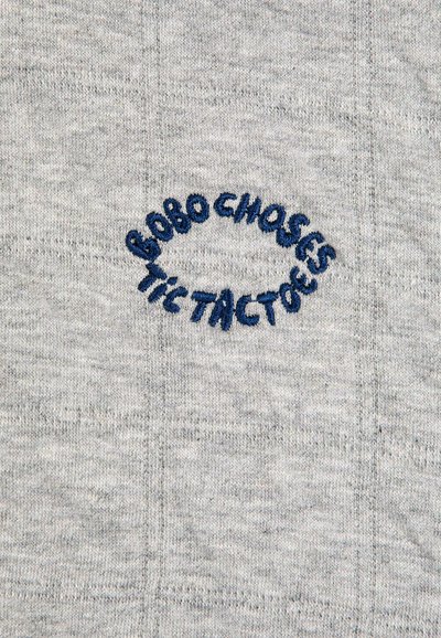 Testo ricamato blu che dice "BOBO CHOSES TIC TAC TOES" curvato su uno sfondo di tessuto lavorato a maglia grigio chiaro.