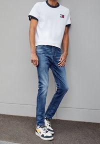 Bílé tričko s krátkým rukávem a námořnickými akcenty, modré slim-fit džíny a vícebarevné tenisky s tlustou podrážkou a šněrovacím designem.