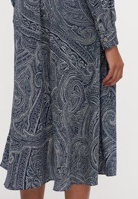 Abito blu navy a maniche lunghe con motivo paisley bianco, caratterizzato da un dettaglio con bottoni sul polsino e un orlo svasato. Tessuto dalla texture morbida.