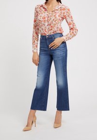Blumenbluse mit langen Ärmeln, auf einem pinken Hintergrund mit orangefarbenen Blumen, kombiniert mit hochtaillierten blauen Jeans im geraden Schnitt und fransigem Saum.