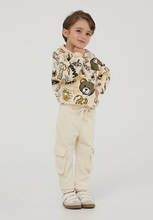 Felpa beige chiaro con stampe di animali e scarabocchi giocosi, abbinata a pantaloni cargo crema con tasche laterali e cintura elastica.
