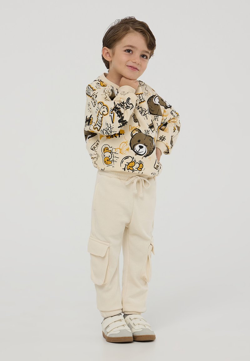 Felpa beige chiaro con stampe di animali e scarabocchi giocosi, abbinata a pantaloni cargo crema con tasche laterali e cintura elastica.