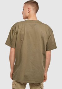 Olijfgroene katoenen T-shirt met korte mouwen, een losse pasvorm en een ronde halslijn, gezien vanuit de rug. Gladde textuur, minimale details.