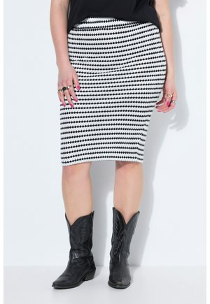 Frau trägt einen schwarz-weiß gemusterten knielangen Rock, schwarzen Oberteil, schwarze bestickte Cowboy-Stiefel und Ringe an beiden Händen.