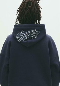 Navy hoodie featuring an embroidered "STWD." logo on the back, with a drawstring hood and relaxed fit. Soft, textured fabric.