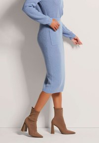 Hellblaues, geripptes Strickkleid mit schmaler Silhouette und Seitentasche. Kombiniert mit braunen, spitzen Ankle-Boots mit blockigem Absatz.