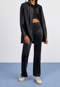 Black satin button-up shirt, black fitted top, and black soft-textured pants. Gray sneakers with a gum sole. Simple design and sleek silhouette.
