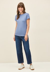 Světle modrý top s krátkým rukávem v kombinaci s tmavě modrými širokými džíny. Model má na sobě bílé tenisky. Hladká textura s volným střihem.