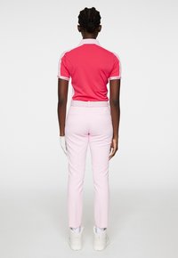 Rosa polo skjorta med vita detaljer och korta ärmar, ihop med ljusrosa byxor. Outfiten har ett bälte och kompletteras av vita skor.