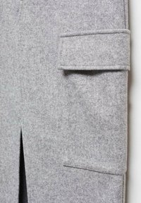 Vêtement en feutre gris avec une poche latérale à rabat, une fente visible à l'ourlet, et une surface lisse et texturée.