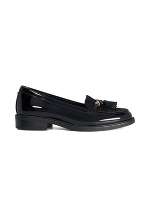 Mocassin en cuir verni noir avec petit talon, détail pompon sur le dessus et panneau texturé sur le cou-de-pied sur fond blanc.