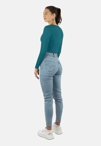Türkiser langärmeliger Cropped-Top, kombiniert mit hellblauen High-Waist-Jeans, die Rückentaschen und eine figurnahe Silhouette haben, getragen mit weißen Sneakers.