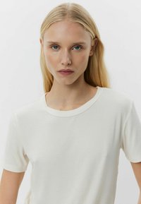 Világos bézs bordás póló kerek nyakkal és rövid ujjakkal, sima tapintással és testhez simuló fazonnal. Egyszerű design.