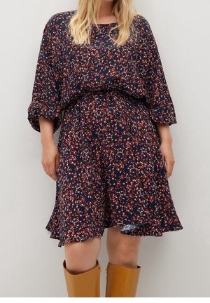 Kobieta w granatowej sukience w kwiaty z rękawami do połowy ramienia, w połączeniu z beżowymi, skórzanymi kozakami sięgającymi do kolan.