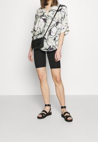 Blus med blommönster i lätt tyg, ihopparad med svarta cykelbyxor och svarta sandaler med remmar. Liten svart axelväska.