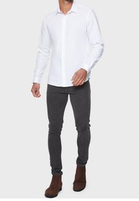 Witte lange mouwen knoopshirt met een kraag. Gecombineerd met grijze slim-fit jeans en bruine suède enkellaarsjes. Soepele stof.