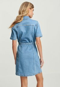 Denim Hemdkleid mit kurzen Ärmeln, tailliertem Schnitt und gürtelspezifischem Design. Hellblaue Farbe und sichtbare Nähte verleihen dem Look ein besonderes Flair.