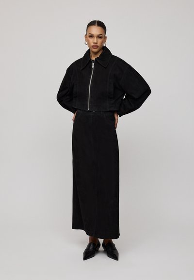 Čierna skrátená bunda na zips s nadrozmernými rukávmi a veľkým golierom, doplnená o zodpovedajúcu dlhú, priliehavú sukňu. Hladká textura.
