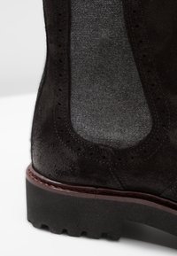 Stivale alla caviglia in suede nero con un pannello di accentuazione grigio, punta arrotondata, perforazioni decorative e suola in gomma testurizzata.