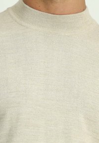 Beżowy sweter z golfem, wykonany z prążkowanej tkaniny, charakteryzujący się wysokim kołnierzem i gładką teksturą, z delikatnymi różnicami w materiale.